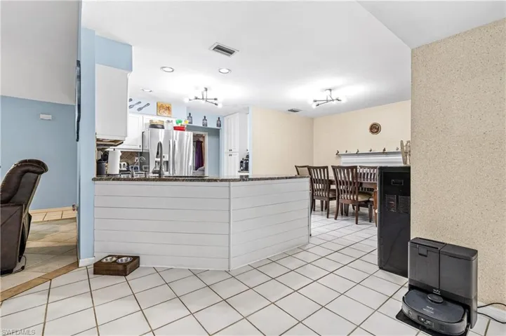 Kitchen with a peninsula, white cabinetry, stainless steel fridge, dark stone counters, and light tile patterned floors