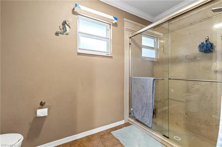 Full bath featuring tile patterned floors, a stall shower, healthy amount of natural light, and ornamental molding
