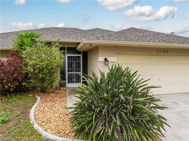 View of exterior entry featuring roof with shingles, a garage, and stucco siding