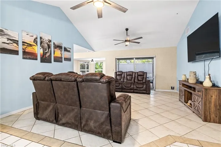 Living room featuring vaulted ceiling, light tile patterned floors, and a ceiling fan