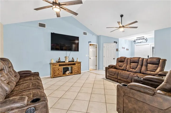 Living room featuring ceiling fan, lofted ceiling, and light tile patterned flooring