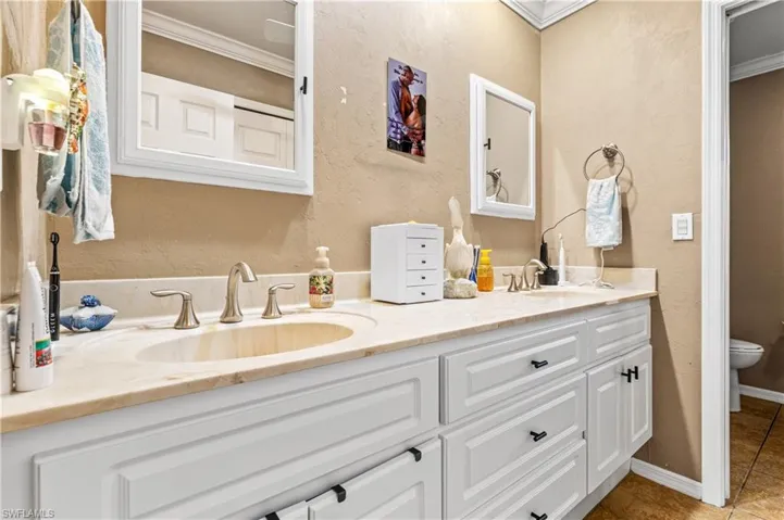 Full bath featuring a textured wall, double vanity, crown molding, and light tile patterned flooring