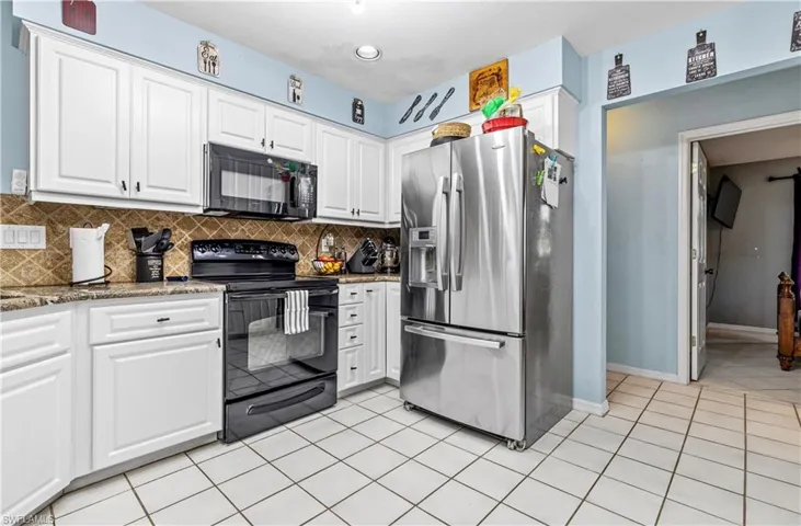 Kitchen with white cabinetry, black appliances, dark stone counters, decorative backsplash, and light tile patterned floors