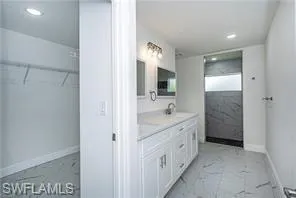 Full bath featuring double vanity, light marble finish flooring, a walk in closet, and recessed lighting