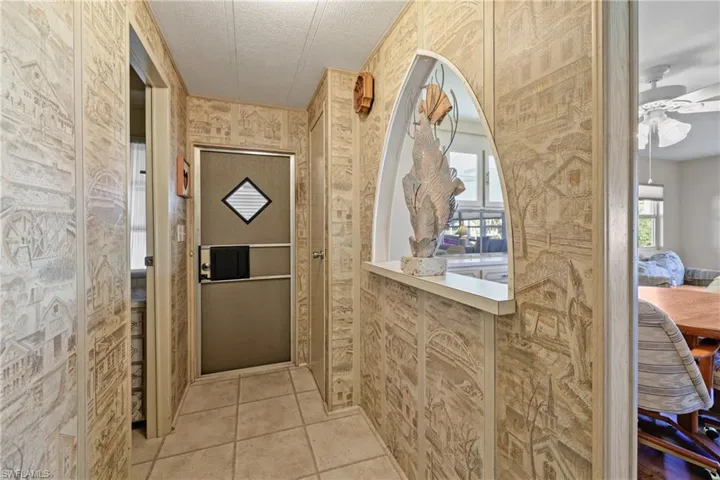 Doorway with ceiling fan, light tile patterned flooring, and a textured ceiling