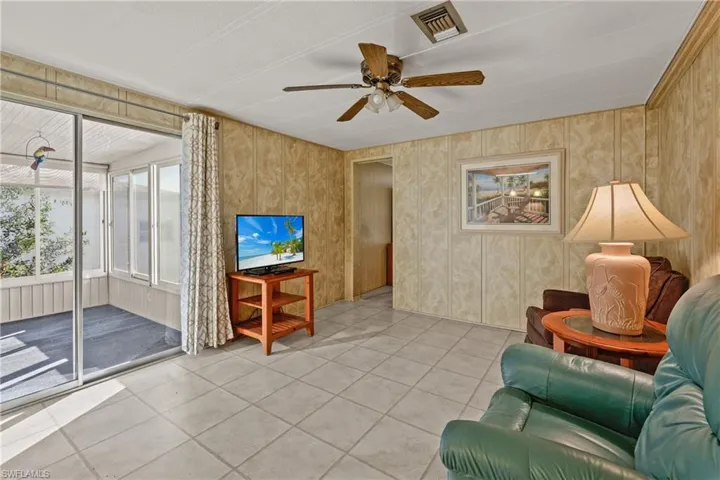 Living room with ceiling fan, light tile patterned flooring, and wooden walls