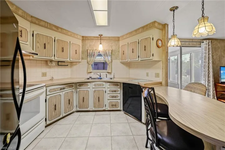 Kitchen featuring white range with electric stovetop, light tile patterned floors, sink, and decorative light fixtures