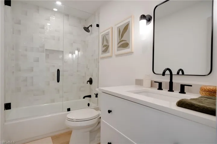 Bathroom with toilet, bath / shower combo with glass door, wood finished floors, and vanity