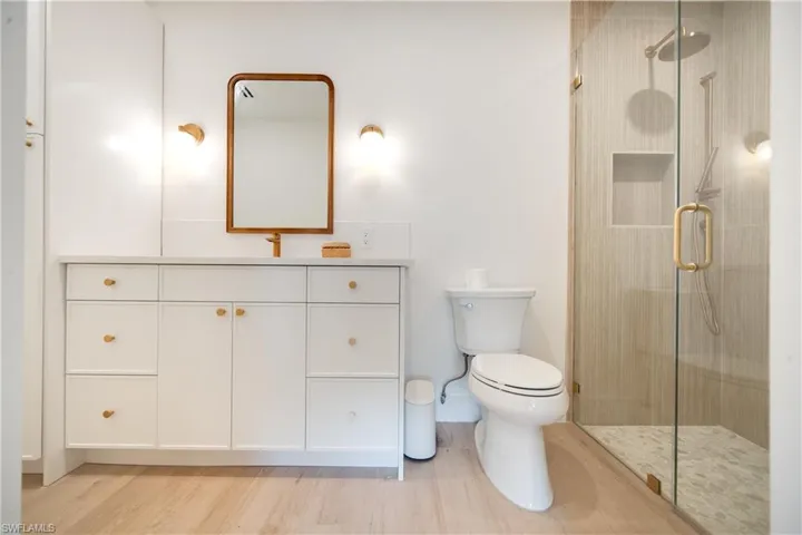 Full bath featuring toilet, a stall shower, wood finished floors, and vanity