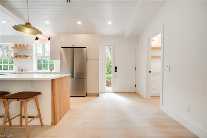 Kitchen featuring a kitchen breakfast bar, light countertops, freestanding refrigerator, open shelves, and beamed ceiling