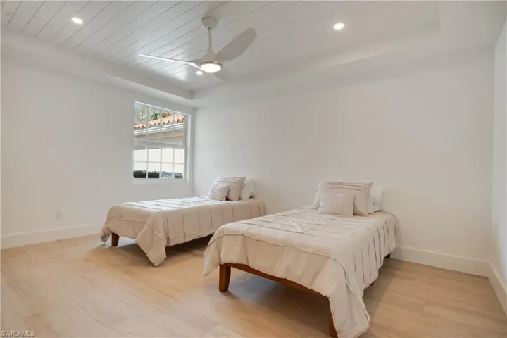 Bedroom with light wood finished floors, baseboards, a raised ceiling, a ceiling fan, and recessed lighting