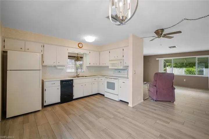 Kitchen with light hardwood / wood-style flooring, a healthy amount of sunlight, ceiling fan with notable chandelier, and white appliances