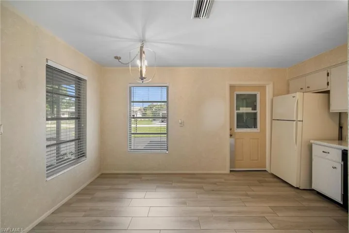 Kitchen featuring white fridge, light wood-type flooring, hanging light fixtures, and white cabinets