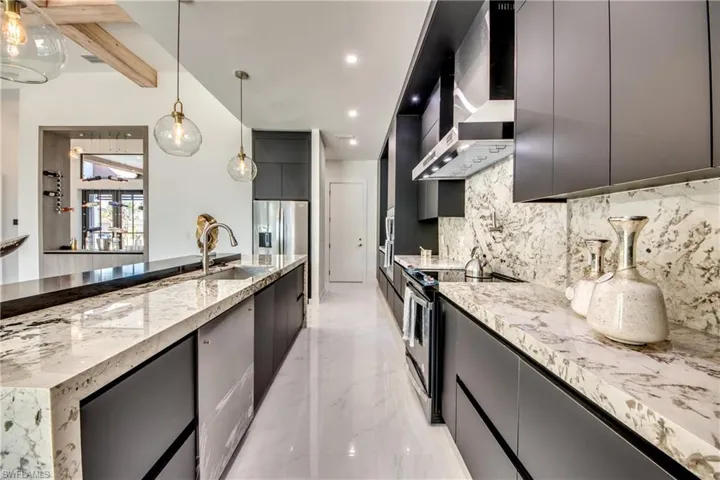 Kitchen with beam ceiling, hanging light fixtures, wall chimney range hood, decorative backsplash, and appliances with stainless steel finishes