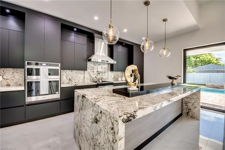 Kitchen featuring backsplash, decorative light fixtures, wall chimney exhaust hood, a large island, and stainless steel appliances