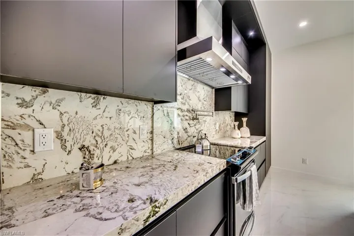 Kitchen featuring light stone countertops, tasteful backsplash, wall chimney exhaust hood, and stainless steel range with electric cooktop