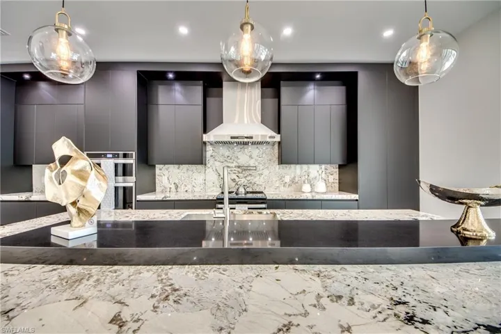 Kitchen featuring backsplash, wall chimney exhaust hood, hanging light fixtures, and appliances with stainless steel finishes
