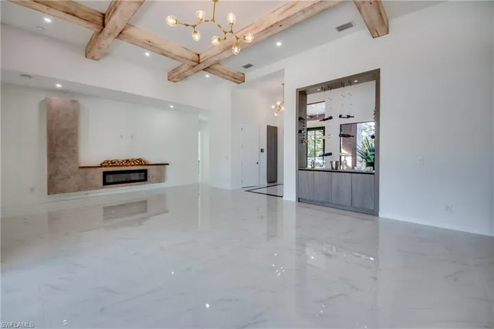 Unfurnished living room featuring beam ceiling, an inviting chandelier, and coffered ceiling