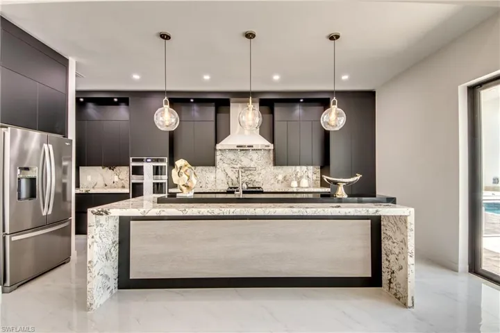 Kitchen with a center island with sink, hanging light fixtures, wall chimney exhaust hood, decorative backsplash, and appliances with stainless steel finishes