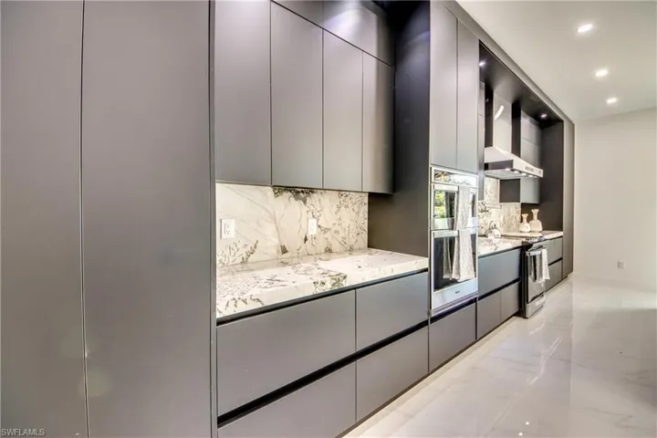 Kitchen with electric range, decorative backsplash, gray cabinets, and wall chimney range hood