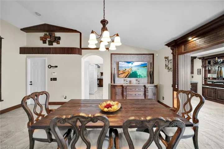 Dining space featuring vaulted ceiling, light tile patterned floors, a chandelier, and arched walkways