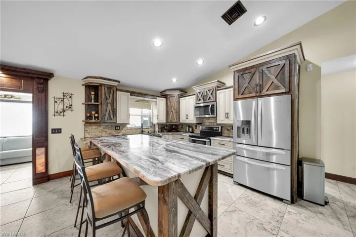 Kitchen featuring light stone counters, stainless steel appliances, decorative backsplash, vaulted ceiling, and a kitchen breakfast bar