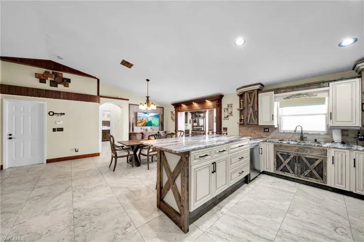 Kitchen with light stone counters, a peninsula, tasteful backsplash, vaulted ceiling, and arched walkways