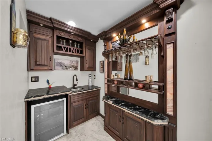 Indoor wet bar featuring dark brown cabinets, beverage cooler, dark stone countertops, open shelves, and stainless steel gas cooktop