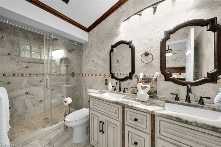 Bathroom with double vanity, crown molding, a shower stall, and tile walls