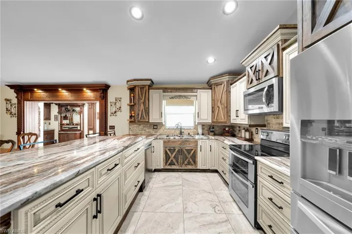 Kitchen featuring cream cabinets, stainless steel appliances, tasteful backsplash, light stone counters, and recessed lighting