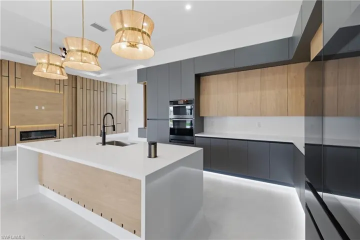Two tone kitchen with modern cabinets, dual tone cabinets, light stone counters, stainless steel appliances, and a center island with sink