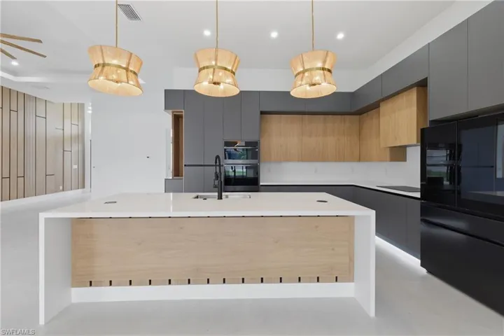 Dual tone kitchen with modern cabinets, decorative light fixtures, two tone cabinetry, an island with sink, and light stone countertops