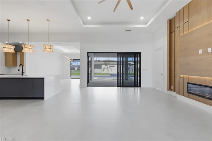 Unfurnished living room with a glass covered fireplace, a ceiling fan, a tray ceiling, and recessed lighting