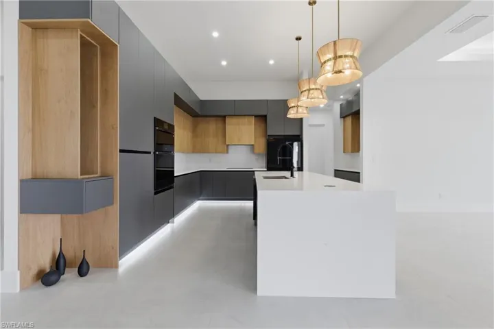 Dual tone kitchen with two tone color scheme, a kitchen island with sink, modern cabinets, pendant lighting, and light stone countertops