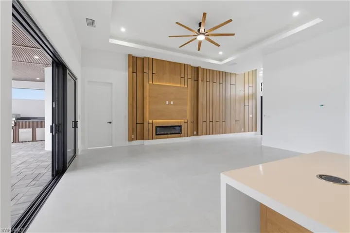 Unfurnished living room with a fireplace, a ceiling fan, recessed lighting, and a tray ceiling