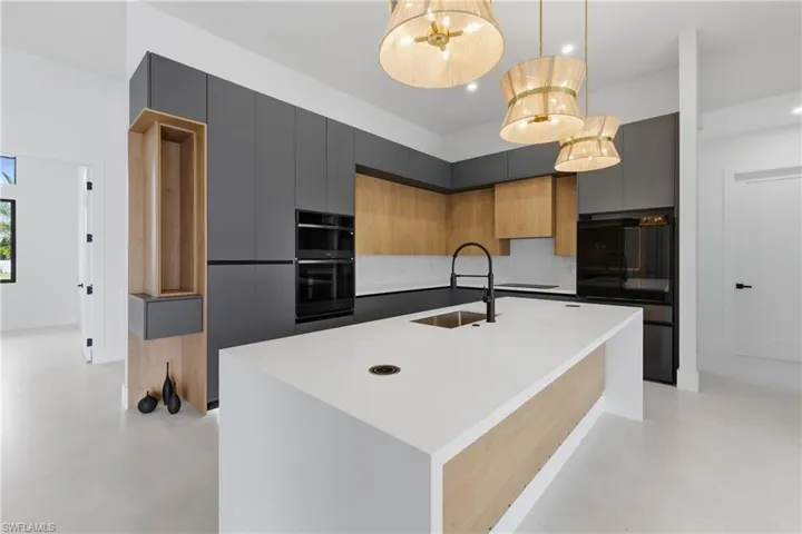Dual tone kitchen with modern cabinets, black appliances, a kitchen island with sink, light stone countertops, and two tone cabinetry