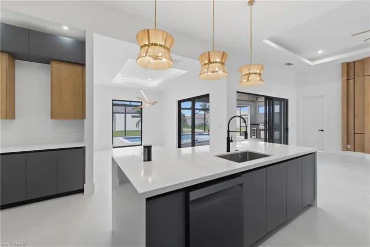 Kitchen with modern cabinets, a tray ceiling, a center island with sink, pendant lighting, and light stone countertops