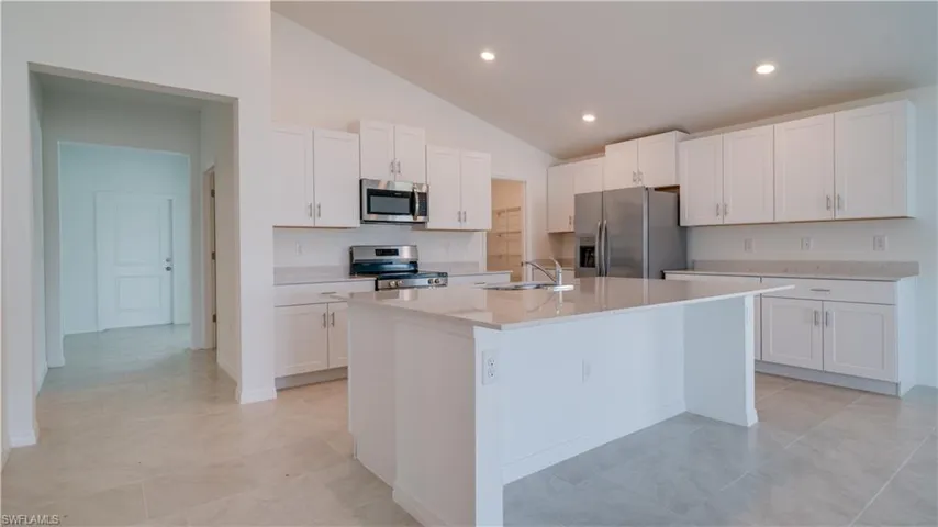 Kitchen featuring vaulted ceiling, white cabinets, stainless steel appliances, an island with sink, and light stone countertops