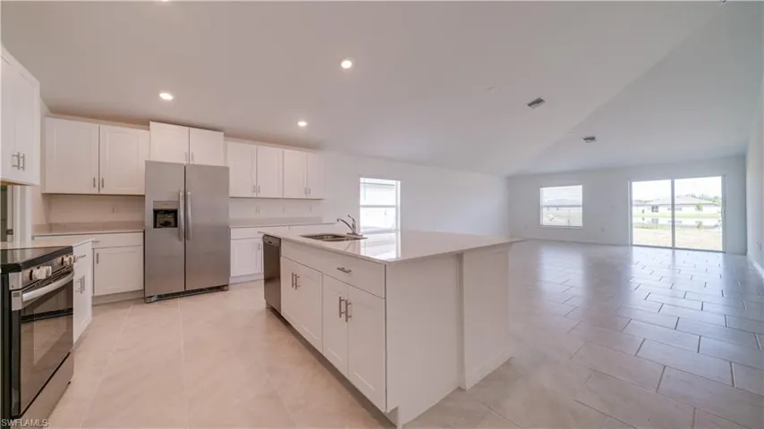 Kitchen featuring stainless steel appliances, white cabinets, a kitchen island with sink, light tile patterned floors, and vaulted ceiling