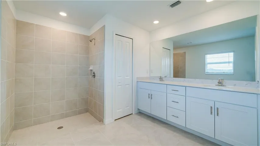 Bathroom with a closet, double vanity, recessed lighting, a tile shower, and light tile patterned floors