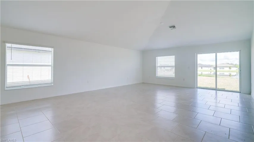 Spare room featuring vaulted ceiling, plenty of natural light, and light tile patterned floors