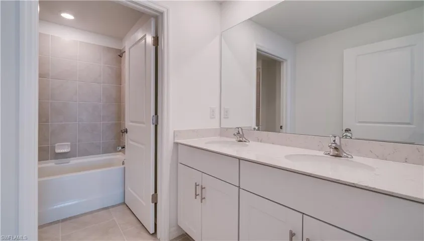 Bathroom with double vanity, light tile patterned floors, and tub / shower combination