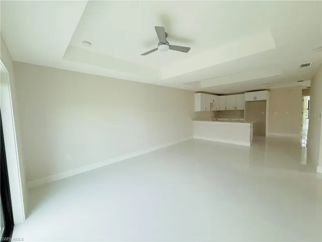 Unfurnished living room featuring a tray ceiling, ceiling fan, and light tile patterned flooring