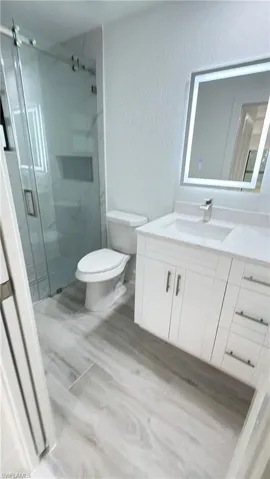 Bathroom with vanity, a textured wall, a marble finish shower, and light wood-style floors
