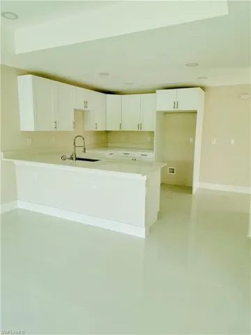 Kitchen featuring white cabinets, a peninsula, light tile patterned flooring, and light stone countertops