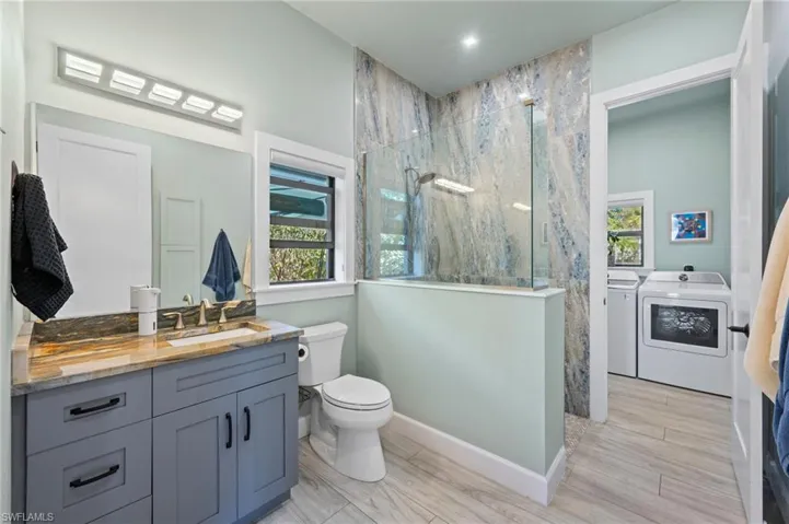 Bathroom featuring a marble finish shower, vanity, washer and clothes dryer, and wood tiled floors