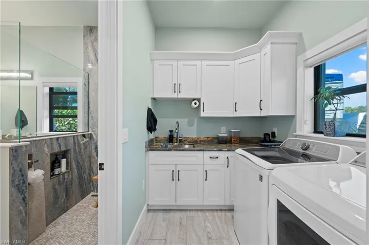 Laundry area with healthy amount of natural light, washer and dryer, light wood-type flooring, and cabinet space