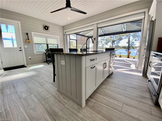 Kitchen featuring white cabinetry, a center island with sink, a kitchen breakfast bar, dark stone counters, and wood tiled floors
