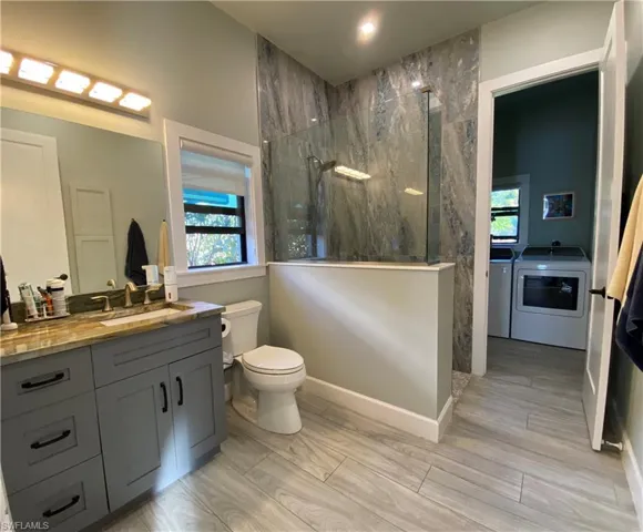 Bathroom featuring a marble finish shower, vanity, washing machine and clothes dryer, and wood finish floors