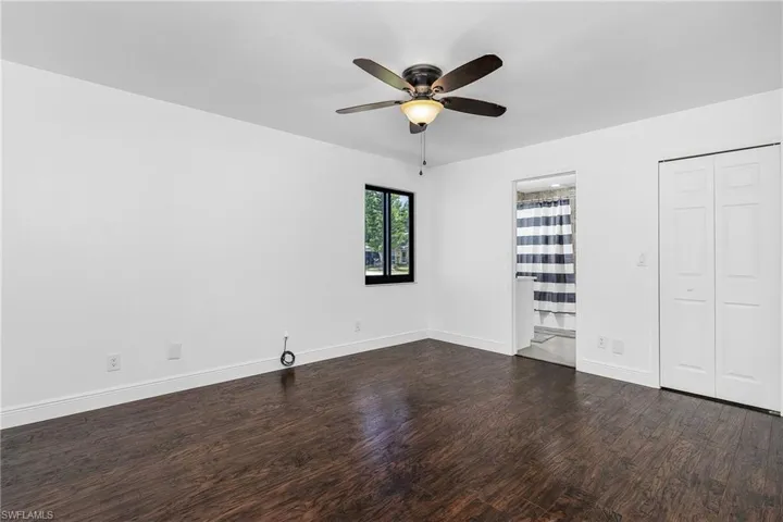 Unfurnished bedroom with ceiling fan, ensuite bath, and dark wood-type flooring